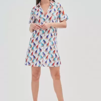 Vestido curto estampado com veleiros multicoloridos, modelo com sapatos pretos em fundo branco.