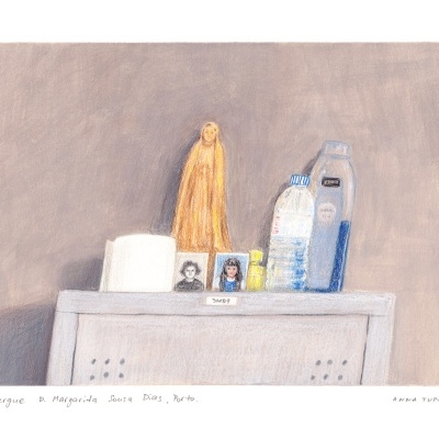 altar com figura de madeira amarela, garrafa de água, frasco amarelo, fotografias e vela branca sobre superfície cinzenta