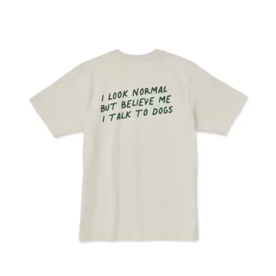 T-shirt bege com texto verde escuro 'I LOOK NORMAL BUT BELIEVE ME I TALK TO DOGS'