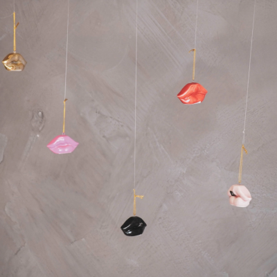 Cinco objetos pendurados em forma de lábios coloridos contra parede cinzenta