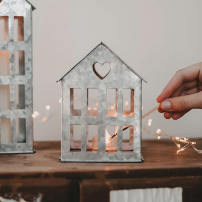 Lanterna decorativa metálica em forma de casa com vela acesa e recortes em janelas e coração