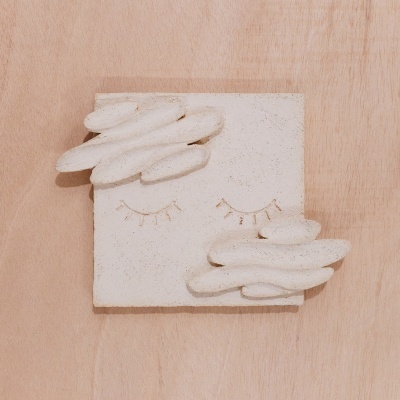 Escultura decorativa abstrata em pedra clara com olhos fechados e nuvens sobre madeira