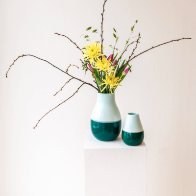 Dois jarros de cerâmica azul-turquesa e branco com flores e ramos secos sobre pedestal branco