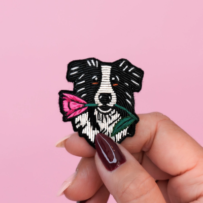 Patch bordado de cão com flor na boca segurado por mão com unhas pintadas