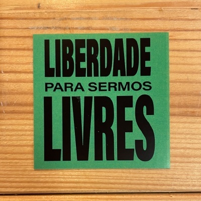 Adesivo verde com texto preto 'LIBERDADE PARA SERMOS LIVRES' sobre madeira clara