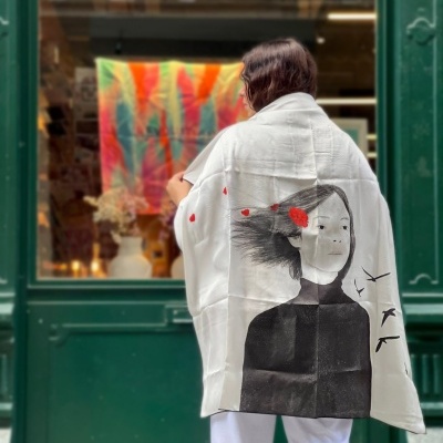 Xale branco com desenho de rosto feminino e detalhes vermelhos usado por pessoa em rua