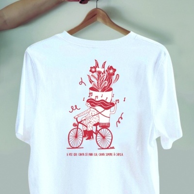 T-shirt branca com estampa vermelha de personagem surreal numa bicicleta e texto em português.