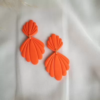 Brincos laranja em forma de conchas sobre tecido branco