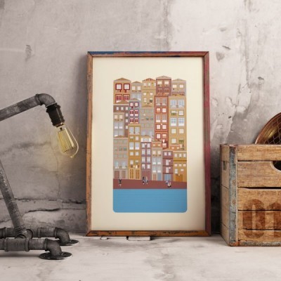 Quadro ilustrativo de edifícios coloridos encostado numa parede cinzenta com textura, perto de luminária e caixa de madeira