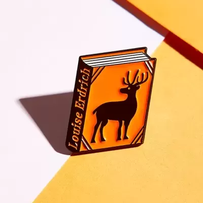 Pin formato livro laranja com cervo e texto Louise Erdrich