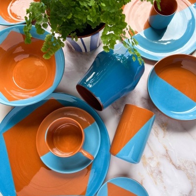 Conjunto de loiça cerâmica azul e laranja com planta verde em vaso