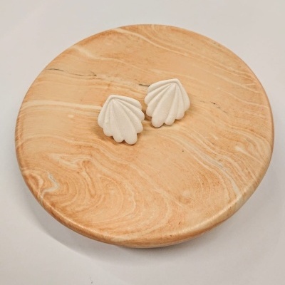 Brincos brancos em forma de concha sobre prato de madeira redondo