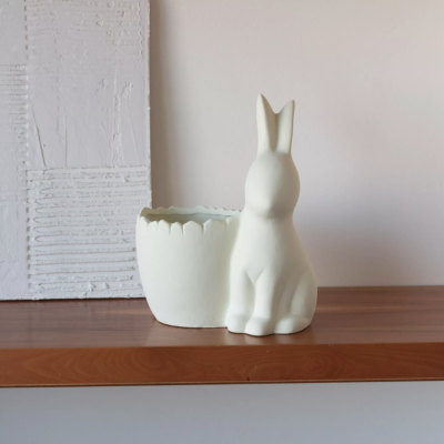 Vaso decorativo branco fosco em forma de coelho sentado ao lado de um vaso oval branco com borda recortada