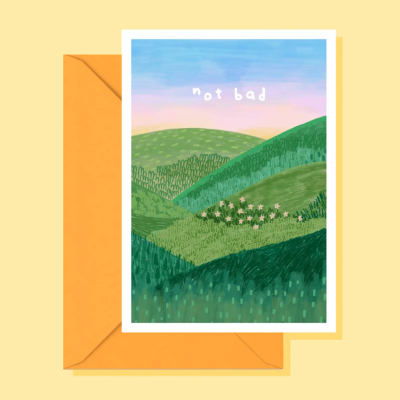 Cartão com ilustração de colinas verdes e texto not bad com envelope amarelo