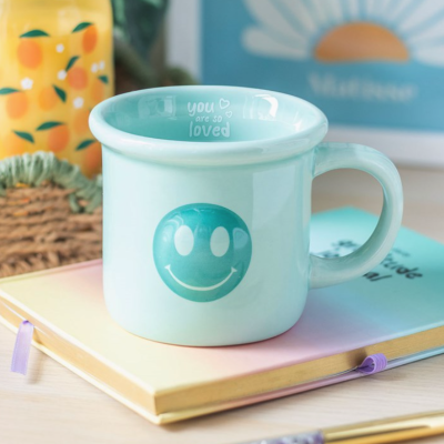 Caneca azul clara com sorriso verde e texto interno sobre livro colorido