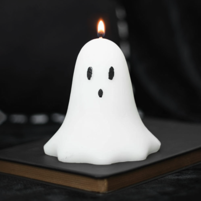 Vela branca em forma de fantasma com olhos e boca a preto, em cima de livro preto.