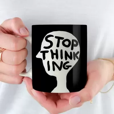 Caneca preta com desenho de cabeça branca e texto STOP THINKING