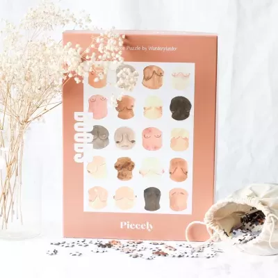 Puzzle ilustrado com rostos diversos em caixa cor de laranja junto a saco branco com peças e flores secas