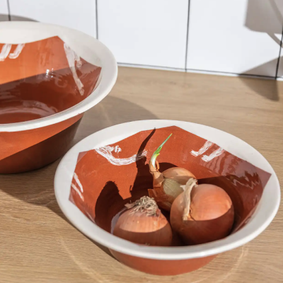 Duas taças de cerâmica terracota com padrão branco, uma com cebolas, sobre mesa de madeira e azulejos brancos