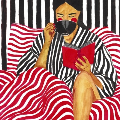 Mulher lendo livro vermelho e bebendo numa chávena preta com fundo e manta de riscas