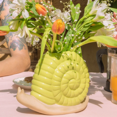 Vaso cerâmico caracol com flores coloridas numa mesa rosa