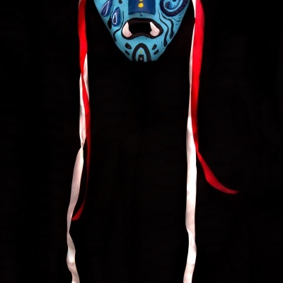 Máscara azul decorada com padrões abstratos e fitas vermelhas e brancas penduradas