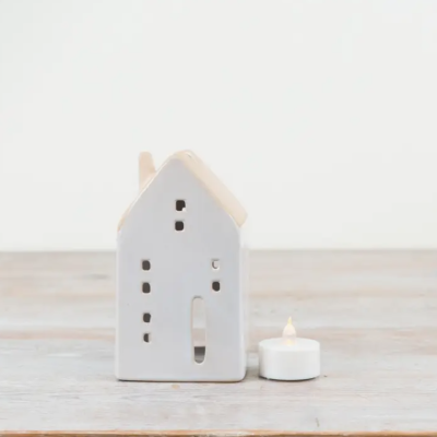 Casa decorativa branca em cerâmica com vela LED ao lado sobre superfície de madeira