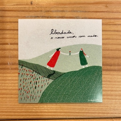 Cartão quadrado com ilustração de duas mulheres trocando uma flor e texto manuscrito em português sobre liberdade.