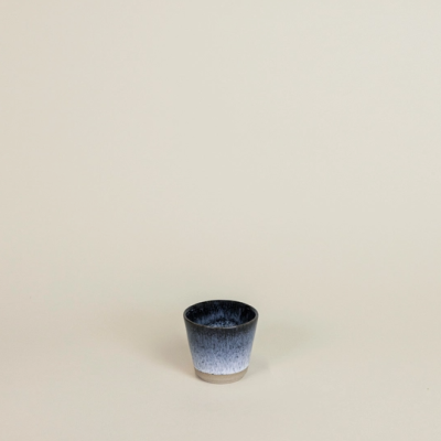 Copo pequeno de cerâmica azul e branco sobre fundo bege