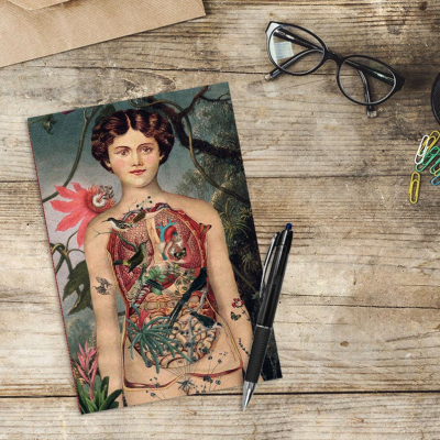Livro com ilustração colorida de mulher com órgãos em destaque sobre mesa de madeira com caneta e óculos