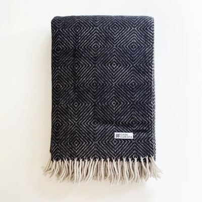 Manta preta dobrada com padrão geométrico, franjas brancas e etiqueta CASA CUBISTA