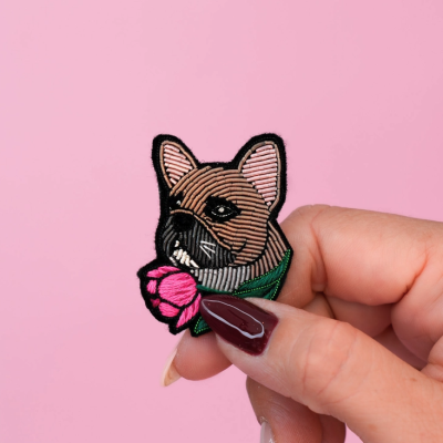 Pedaço bordado com cabeça de cão castanho e flor rosa segurado por mão