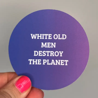 Adesivo roxo redondo com texto branco segurado por mão com unhas rosas