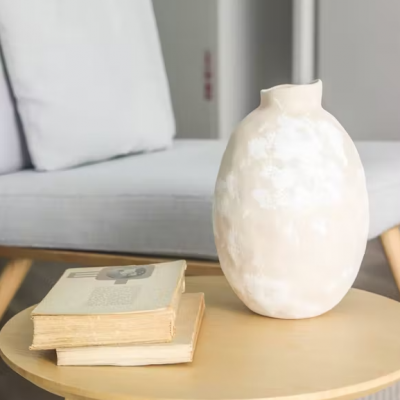 Vaso cerâmico e livros numa mesa redonda de madeira clara em frente a uma cadeira cinza