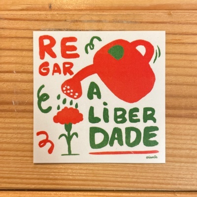 Cartaz com regador vermelho a regar flor vermelha e texto REGAR A LIBERDADE em vermelho e verde