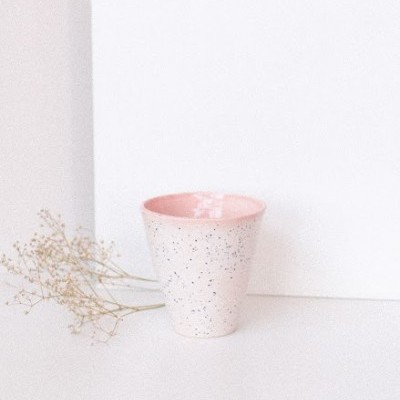 Copo de cerâmica branco com interior rosa e manchas pretas ao lado de flores secas