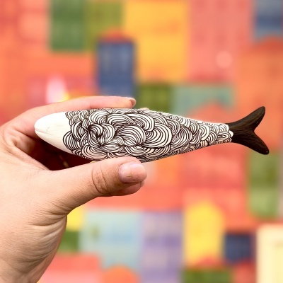 Peixe decorativo de madeira pintada com padrão preto e branco.