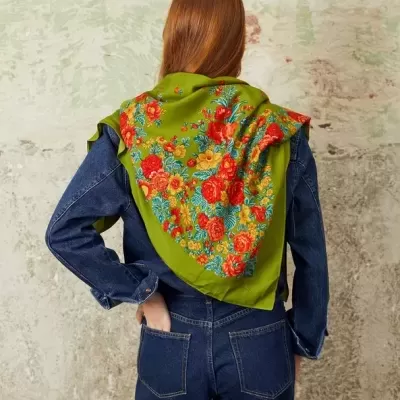 Lenço verde com padrão floral colorido visto atrás, usado com macacão de ganga azul escuro, parede texturada de fundo.