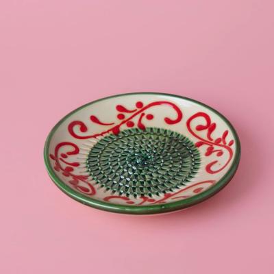 Prato cerâmico decorativo circular com padrão verde e vermelho sobre fundo rosa.