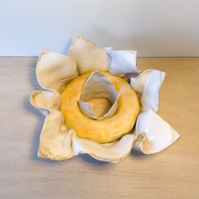 Objeto decorativo em cerâmica creme e amarelo sobre madeira clara