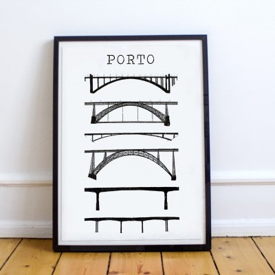 Pôster com desenhos a preto de pontes e palavra PORTO, em moldura preta encostada em parede branca sobre chão de madeira.