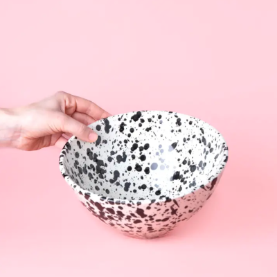 Taça redonda branca com manchas pretas numa mão sobre fundo rosa.