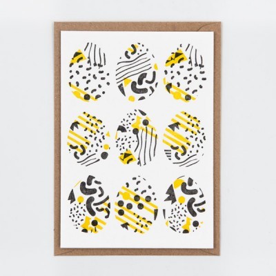Postal com padrão de ovos decorativos em amarelo, preto e branco sobre envelope castanho