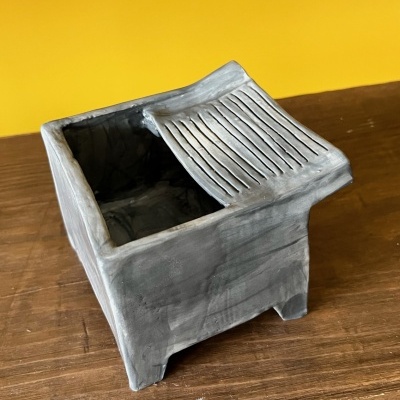 Caixa quadrada cinzenta com tampa deslizante sobre superfície de madeira