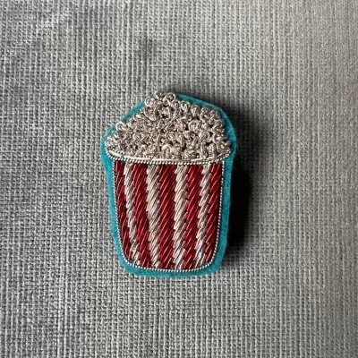 Emblema bordado em forma de balde de pipoca colorido colocado sobre tecido cinza