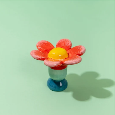 Vaso cerâmico em forma de flor vermelha com centro amarelo e base colorida sobre fundo verde claro