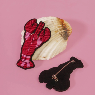 Broche de lagosta feito de miçangas em concha marinha sobre fundo rosa