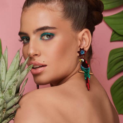 Mulher com brincos coloridos de pássaros e estrelas segurando uma coroa de abacaxi