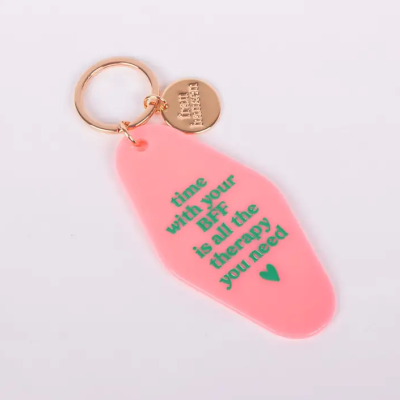 Porta-chaves rosa com texto verde e detalhes metálicos dourados