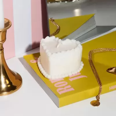 Vela em forma de coração branca sobre livro amarelo com colar e suporte de vela dourado